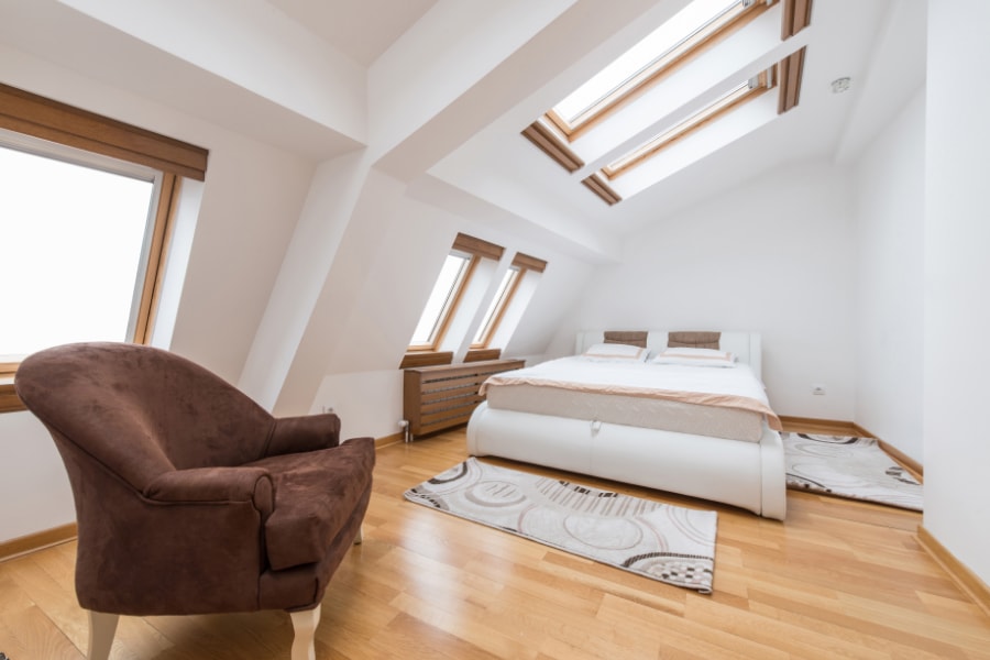 bedroom loft conversion with brown arm chair double bed and oak wood flooring with large windows and roof lights